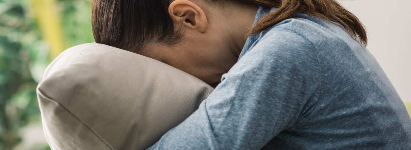 Imagem de mulher abraçando o travesseiro triste pela infertilidade sem causa aparente